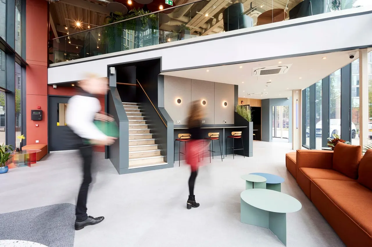 Modern leisure venue interior with two people moving through a multi-level space featuring stairs, bar seating, orange sofa and contemporary furnishings.