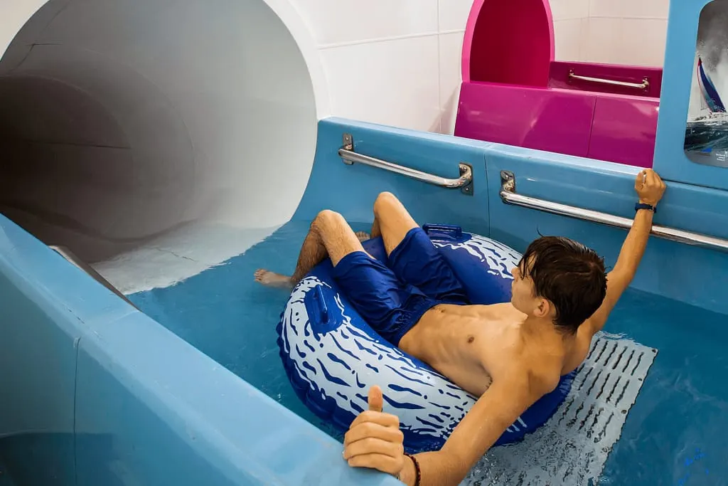 Child sliding down a blue water slide on an inflatable ring at an indoor water park.