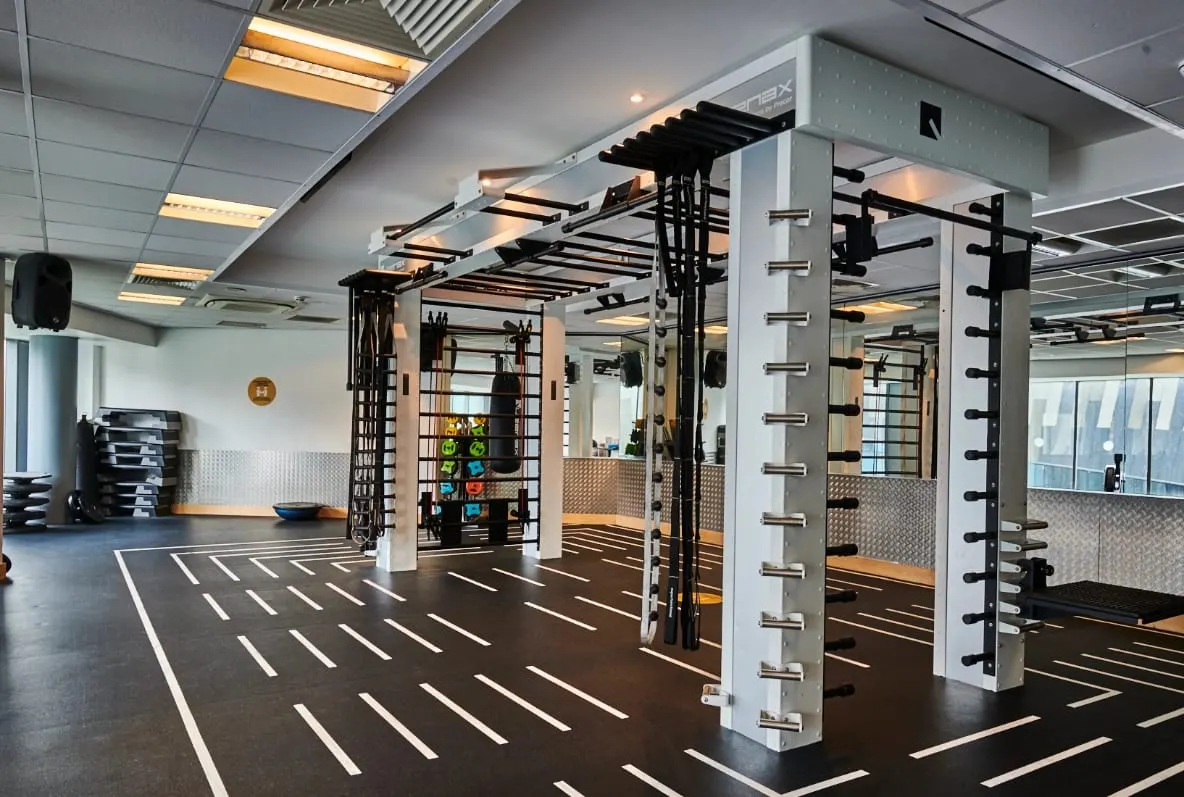Modern gym interior with functional training equipment including racks and bars on dark flooring with white markings.