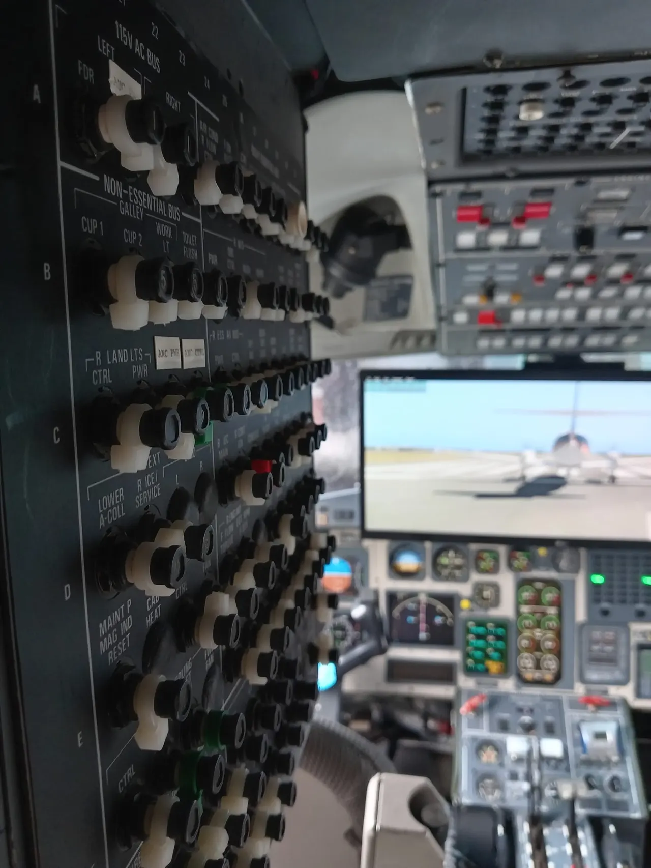 Aircraft flight simulator cockpit with control panels and switches, with runway view displayed on screen.