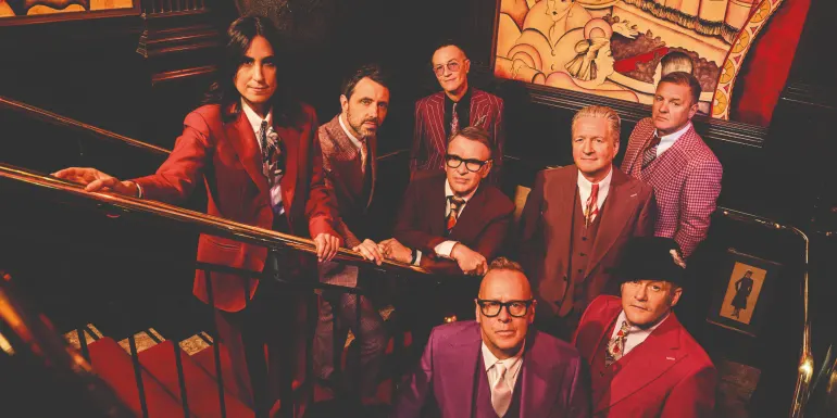 Band members in colourful suits posing on a staircase.