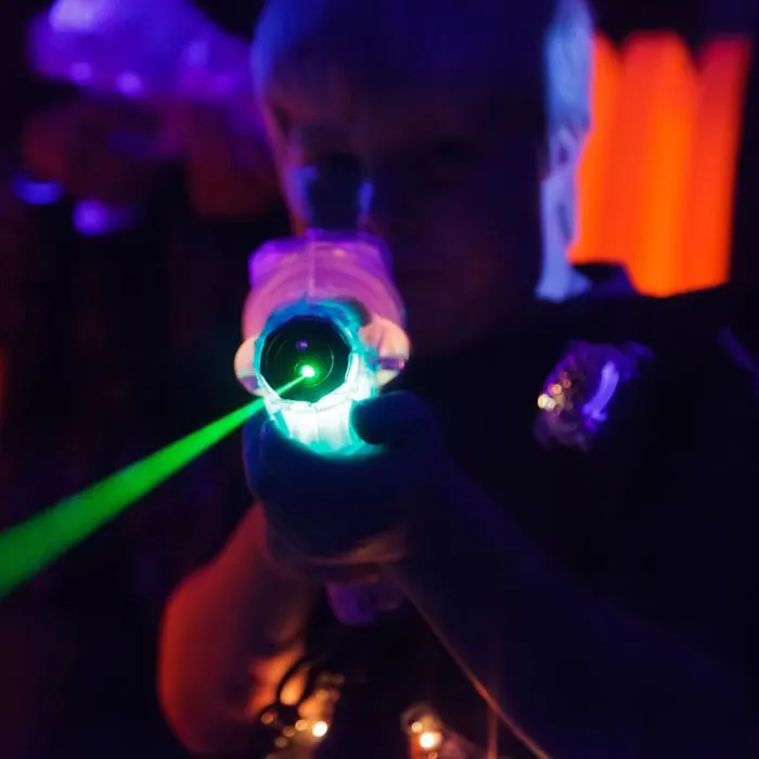Child holding a glowing laser tag gun with neon lights in dark indoor play arena.