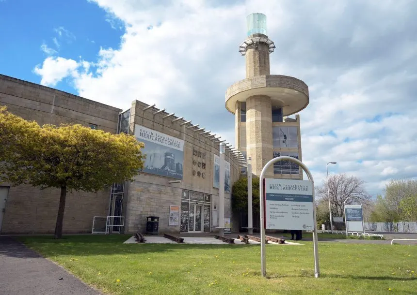 Stone heritage centre building with cylindrical tower and signage on a sunny day with scattered clouds.