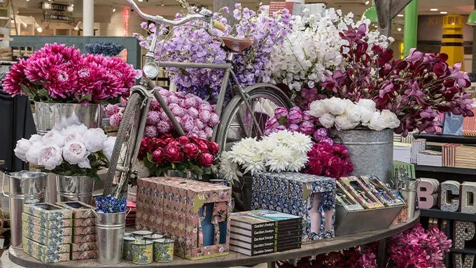 Display of fresh cut flowers in various shades of pink, purple, white and burgundy arranged in containers and vases at a retail venue.