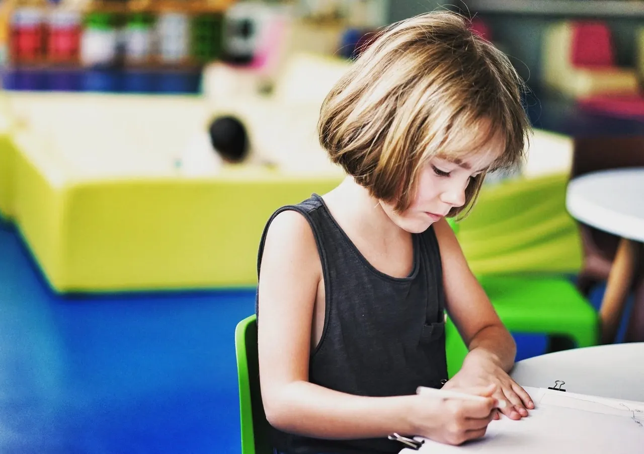 A young child drawing or writing at a table in a colourful indoor play centre.