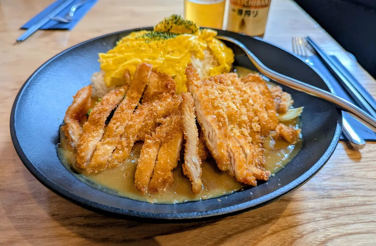 Sliced roasted duck breast with yellow noodles and broccoli on a dark plate, served with beer.