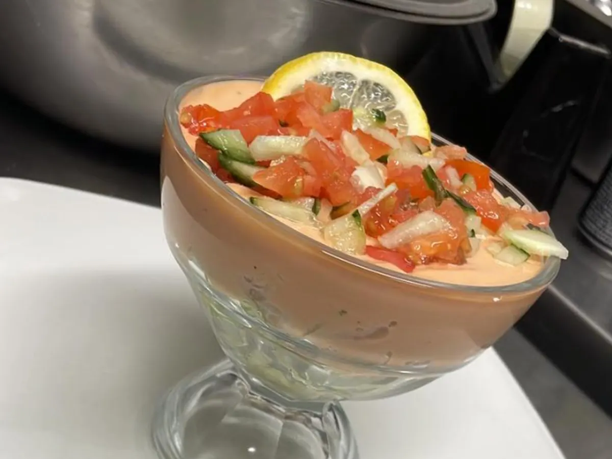 Cocktail garnished with lemon slice and topped with diced tomato and cucumber, served in a coupe glass.