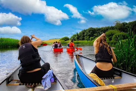 Group of people paddling canoes along a scenic waterway lined with reeds under blue sky.