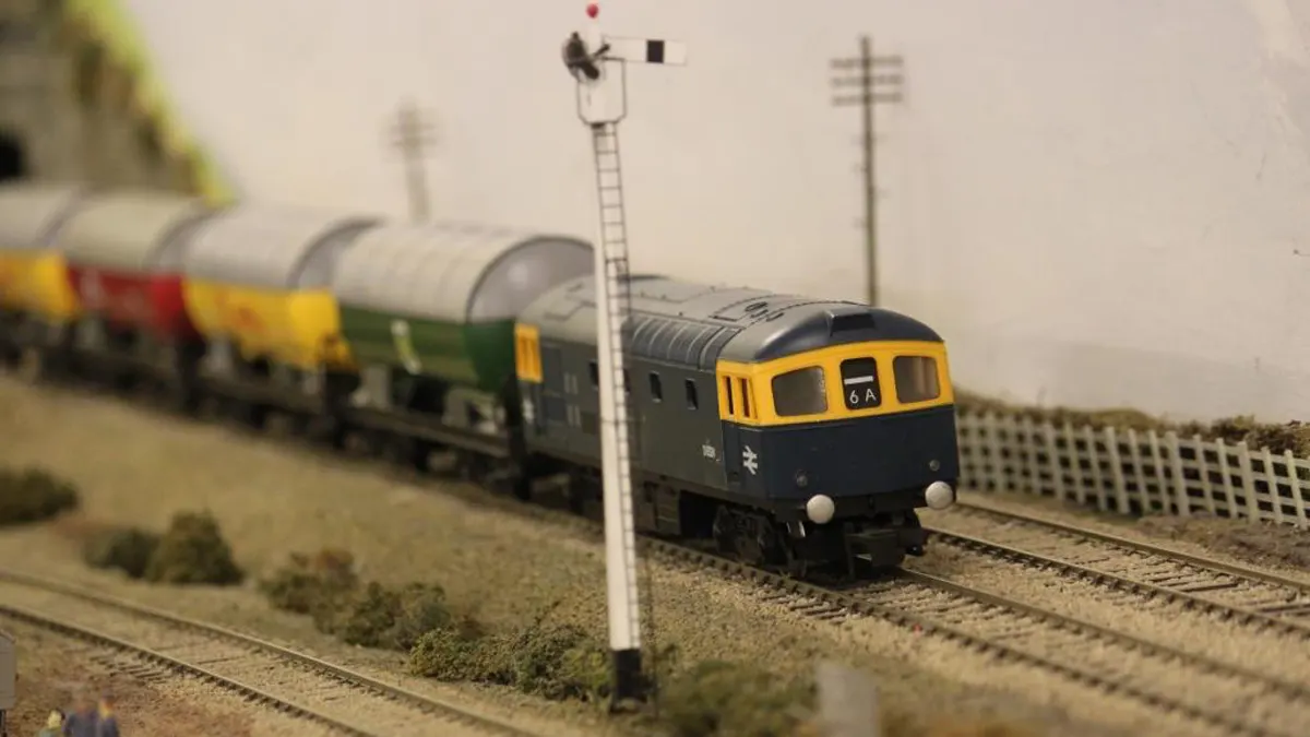 Model train set with miniature diesel locomotive and freight cars on track with signal post.
