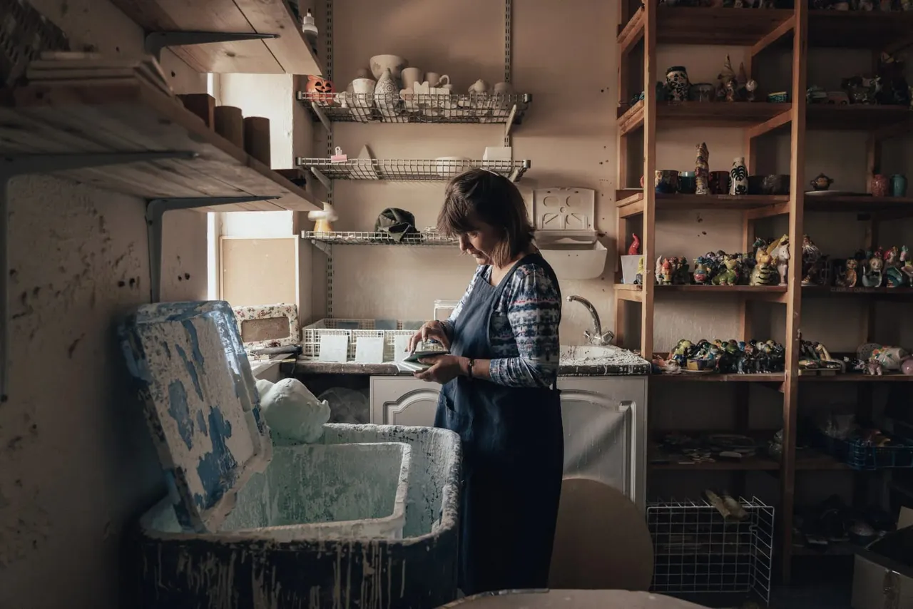 Woman working at pottery studio sink surrounded by shelves displaying ceramic pieces and sculptures.