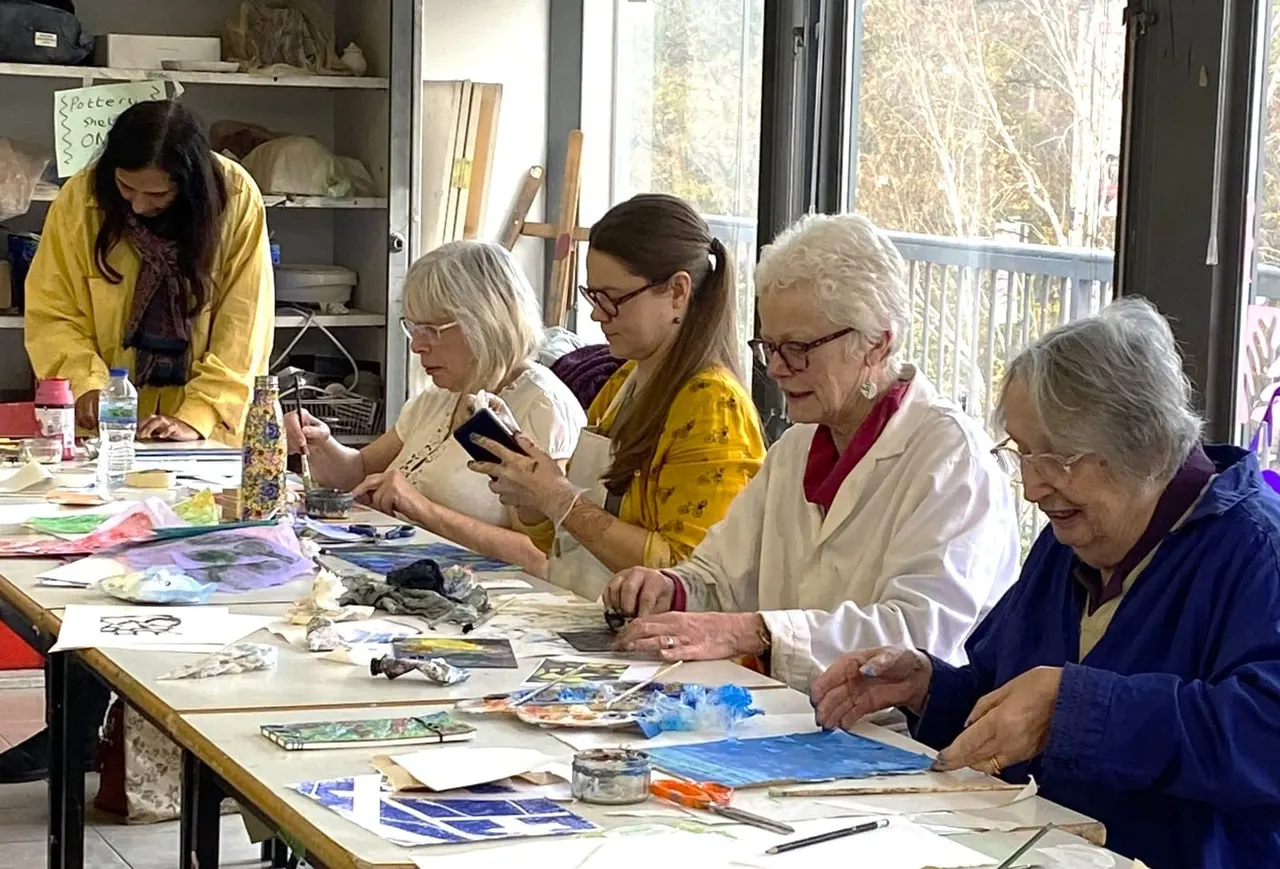 A group of people engaged in a watercolour painting workshop at a table with art supplies and materials spread out.