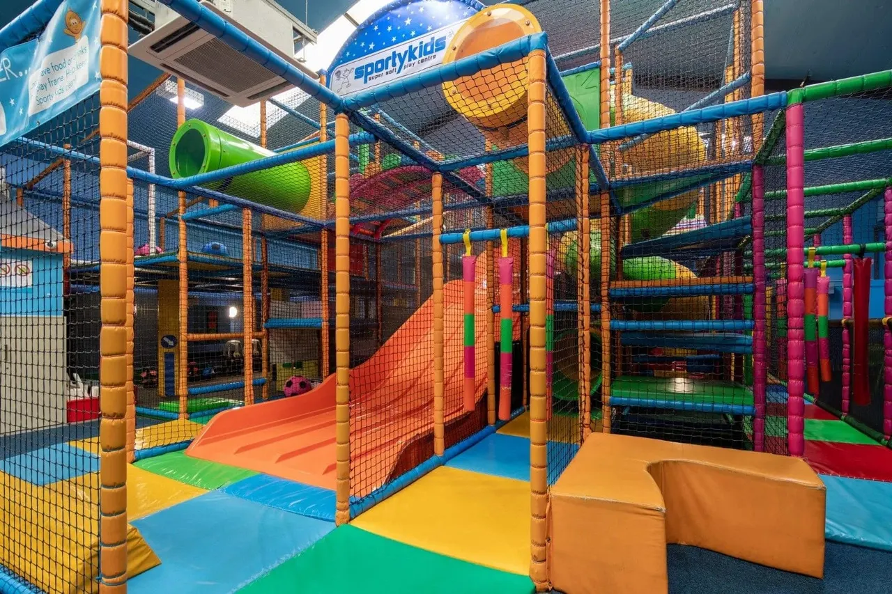 Colourful indoor soft play area with inflatable structures, slides, climbing frames and netting at a children's leisure centre.