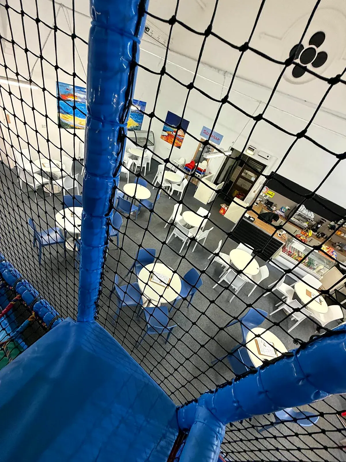 View from inside a large blue inflatable play structure looking down at an indoor play centre with seating and facilities.