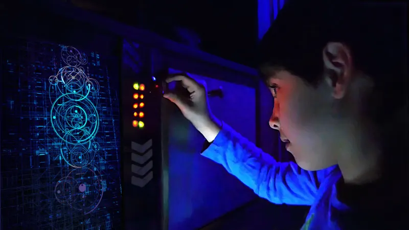 Person interacting with a blue-lit interactive display showing digital circuit designs in a dark room.