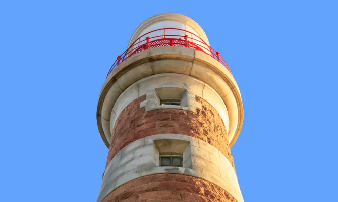 Historic lighthouse tower with red and white striped bands against a clear blue sky.