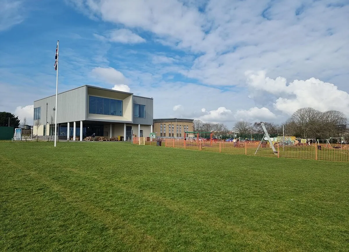 Modern sports facility building with playground fenced area under blue sky with white clouds.