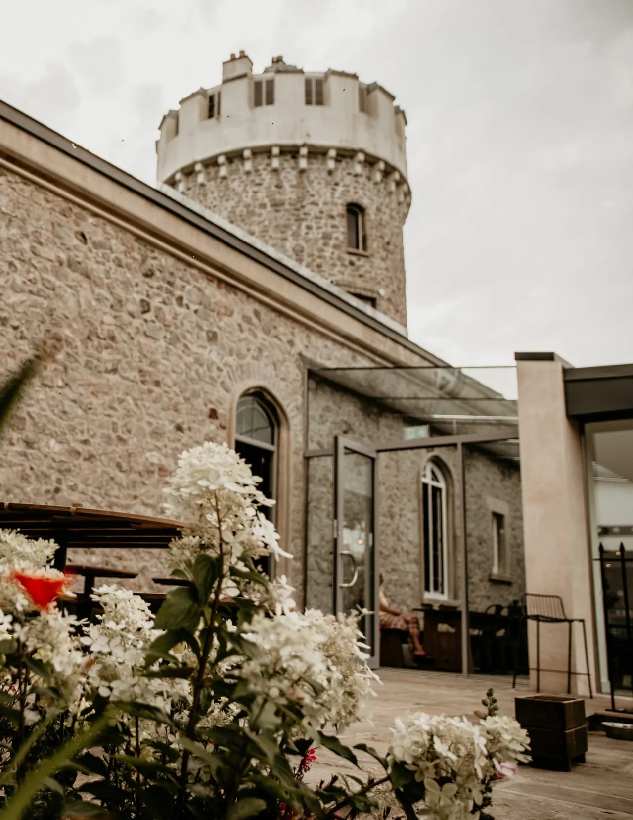 Historic stone tower with crenellated top and white flowers blooming in the foreground courtyard area.