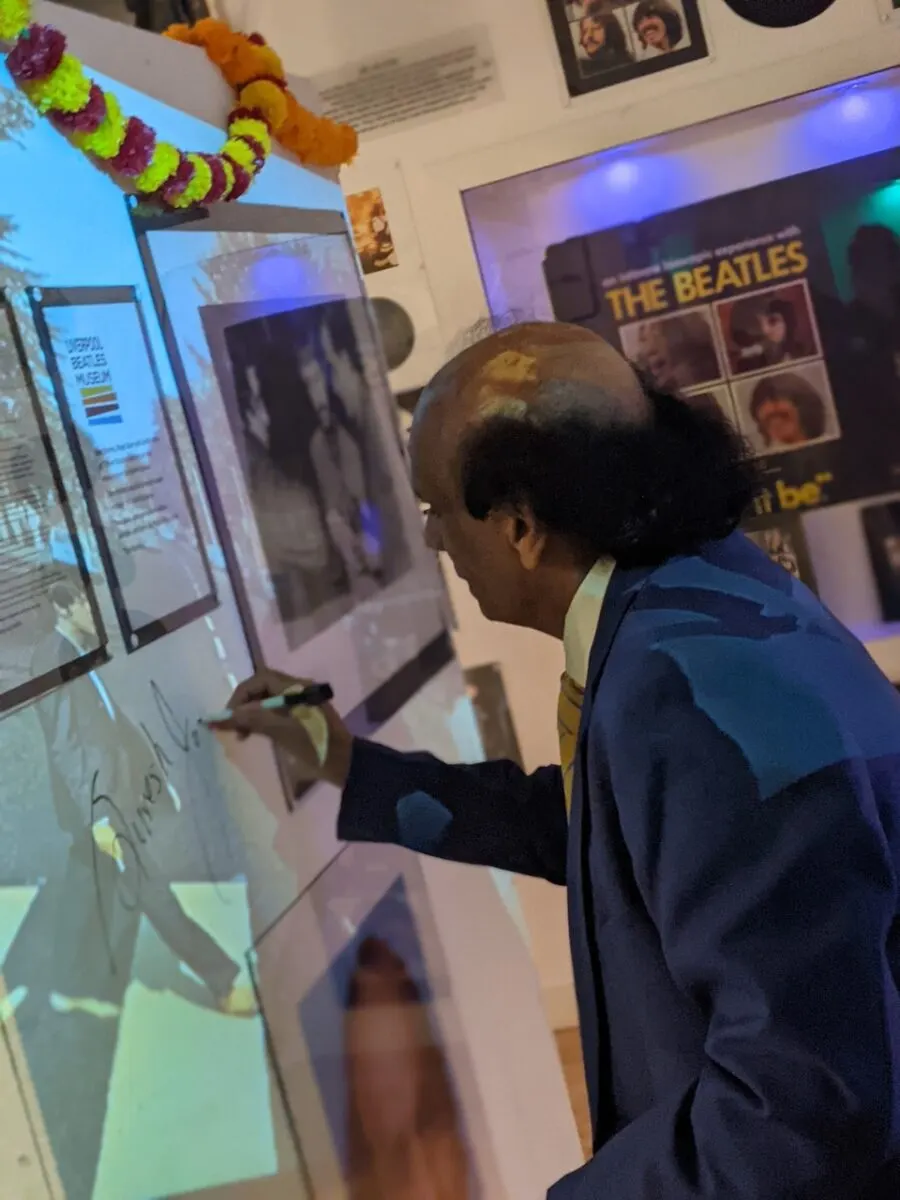 A visitor interacts with an illuminated touchscreen display in a museum exhibition space decorated with colourful garlands.
