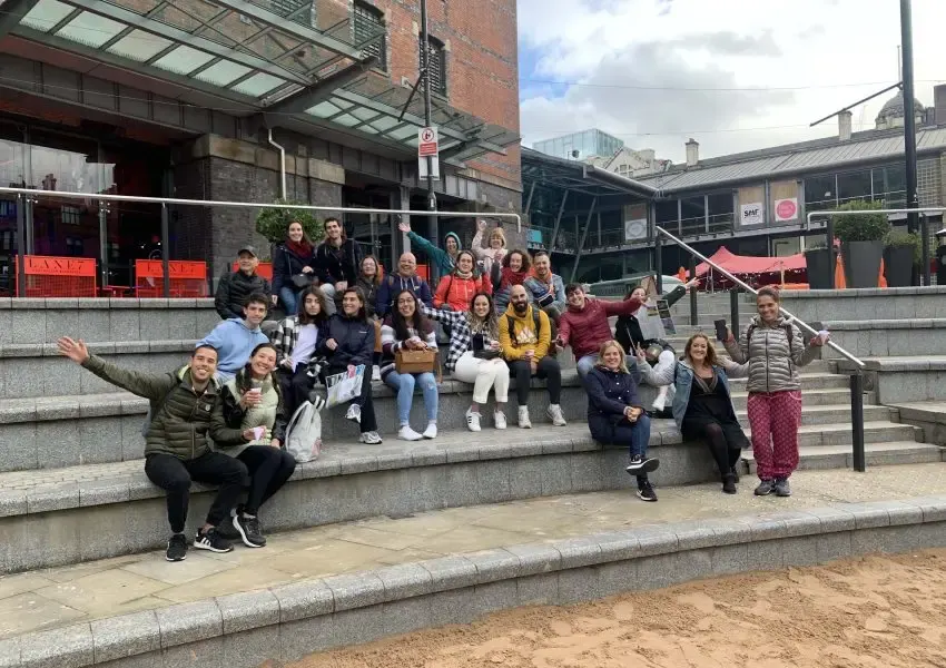 Large group of people posing together on outdoor steps in an urban courtyard setting with brick buildings.
