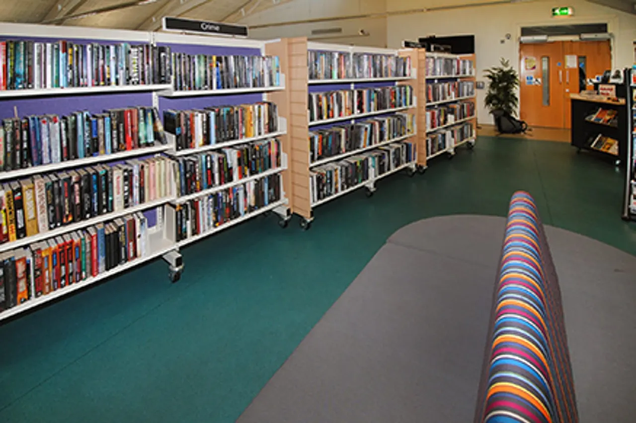 Library media section with shelves of DVDs and films, colourful cushioned seating in foreground.