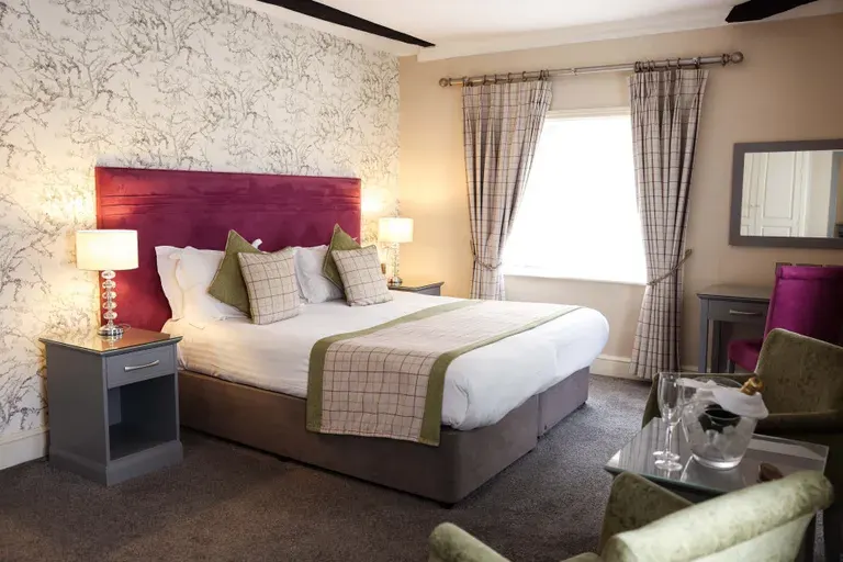 Upmarket hotel bedroom with burgundy headboard, white bedding, green accents, patterned wallpaper and curtains.