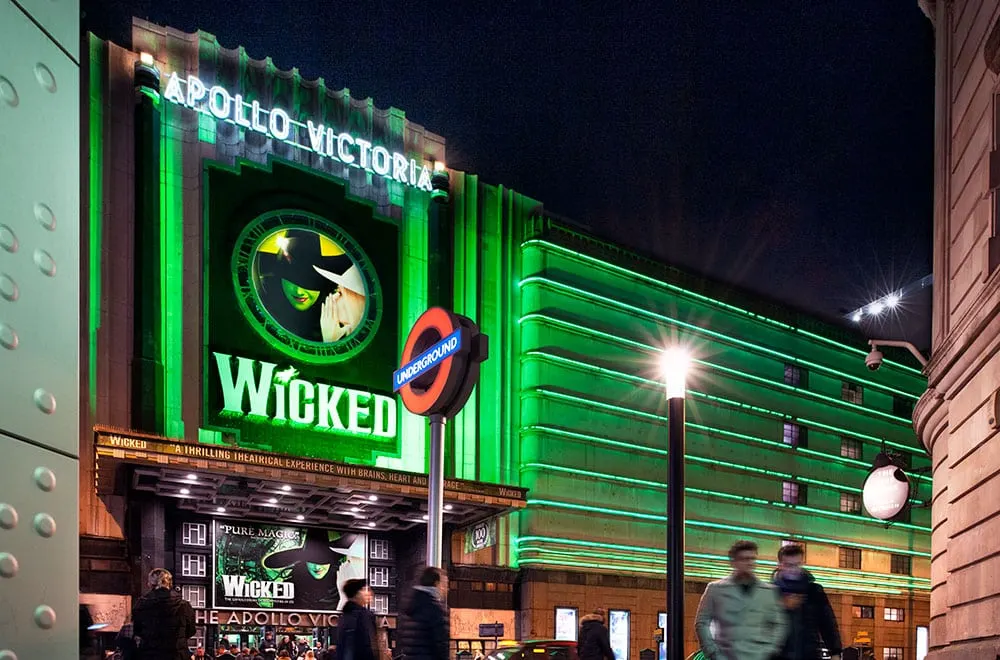 This is a designed graphic — it's a promotional poster/advertisement for a theatrical production displayed on a building exterior.

GRAPHIC