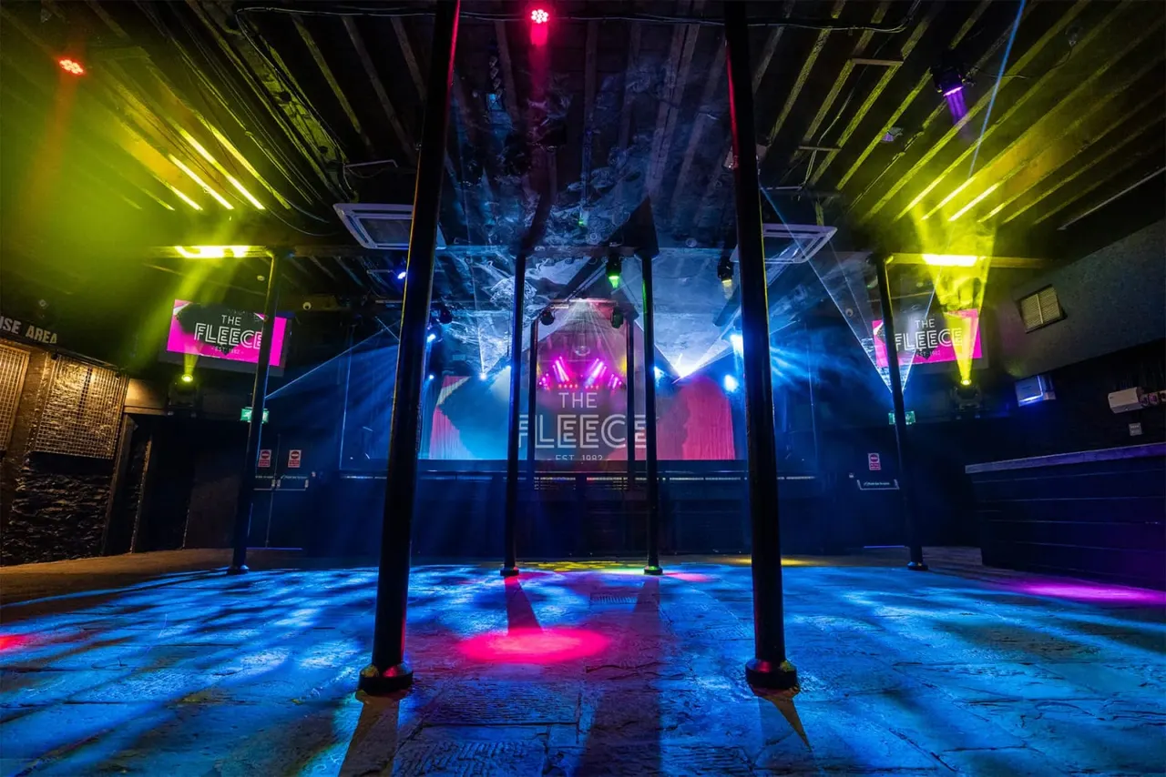 Empty nightclub interior with neon lighting in blue, pink and yellow, illuminated support pillars and signage.