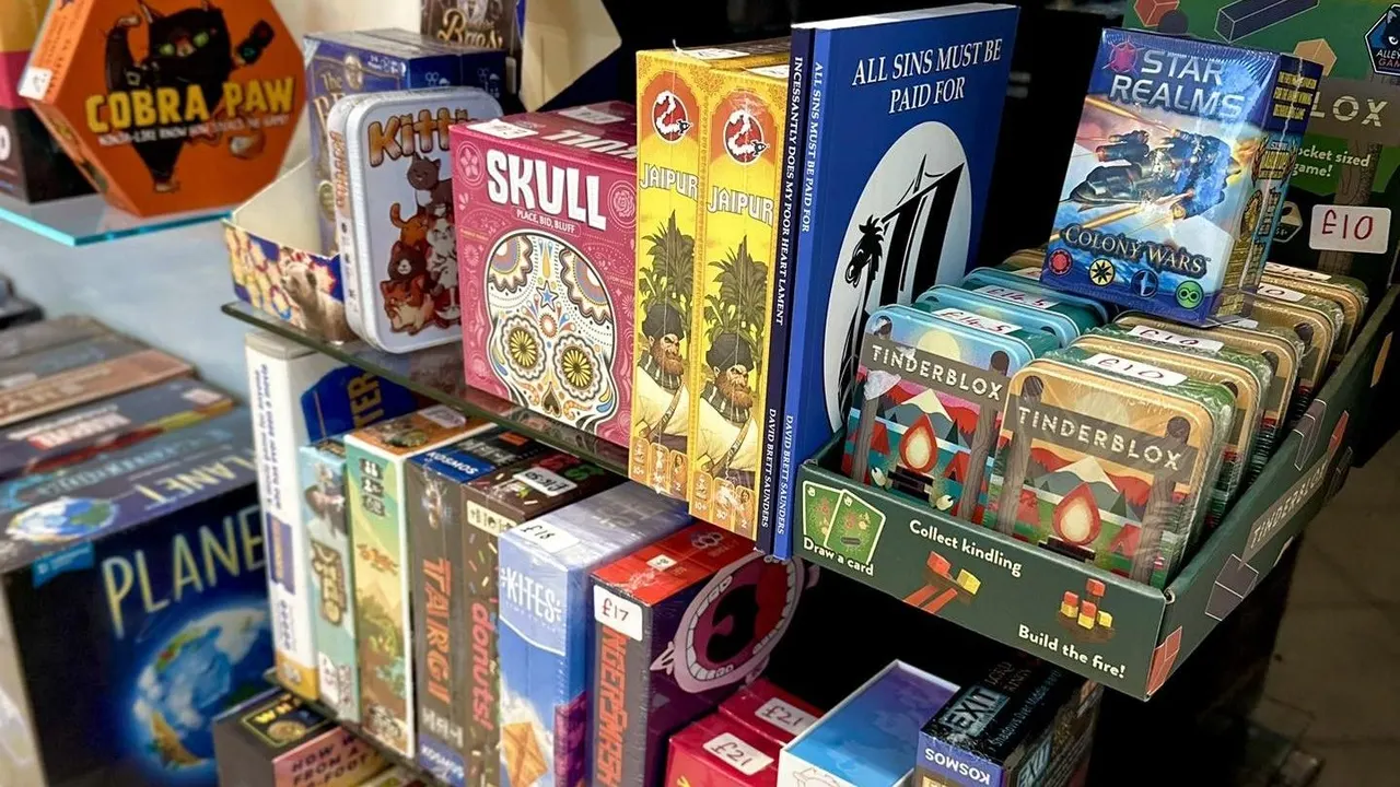 Board games and card games displayed on shelves in a retail setting, including titles like Skull, Jaipur, and Tinderblox.
