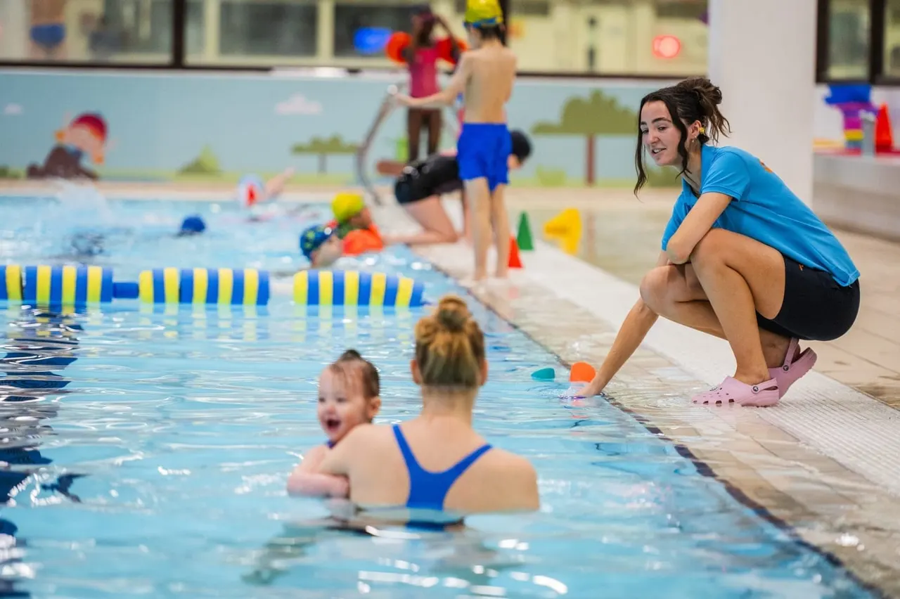 Swimming instructor supervising young children during a swimming lesson in an indoor pool.