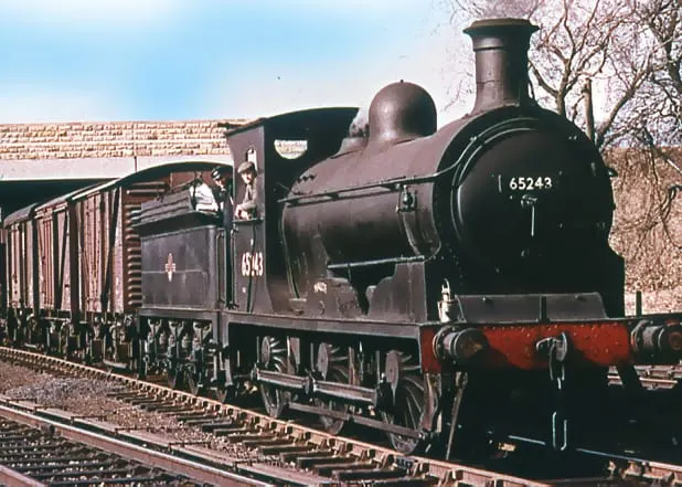A dark green and red steam locomotive numbered 65243 with attached passenger carriages on railway tracks.