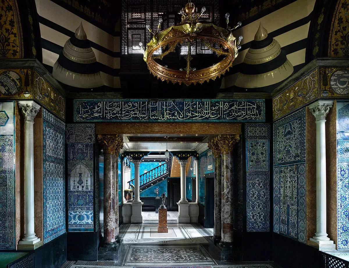 Ornate entrance hall with Islamic tilework, decorative columns, brass chandelier and patterned ceiling in a historic house museum.