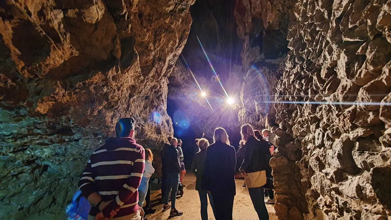 Visitors exploring a cave chamber with dramatic rocky walls lit by bright artificial lighting.