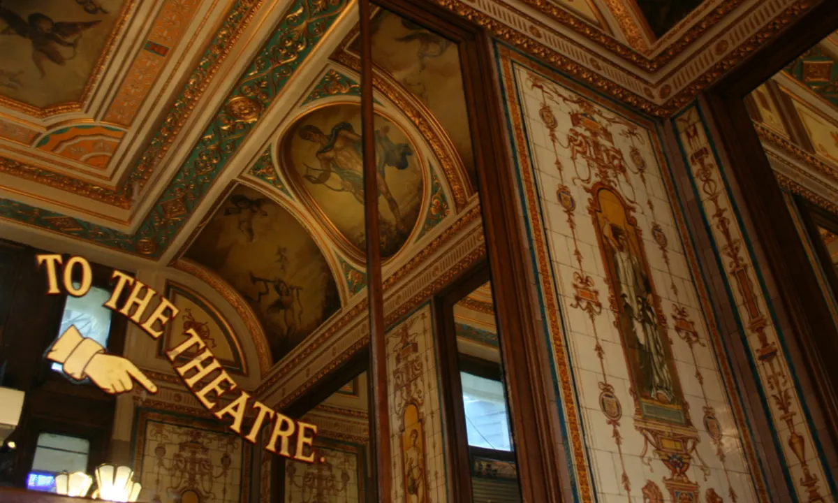 Ornate ceiling with gilded decorative panels, painted medallions and frescoes in a grand theatre interior.