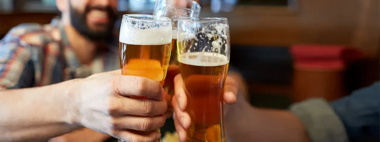 Two people clinking glasses of beer together in a pub.