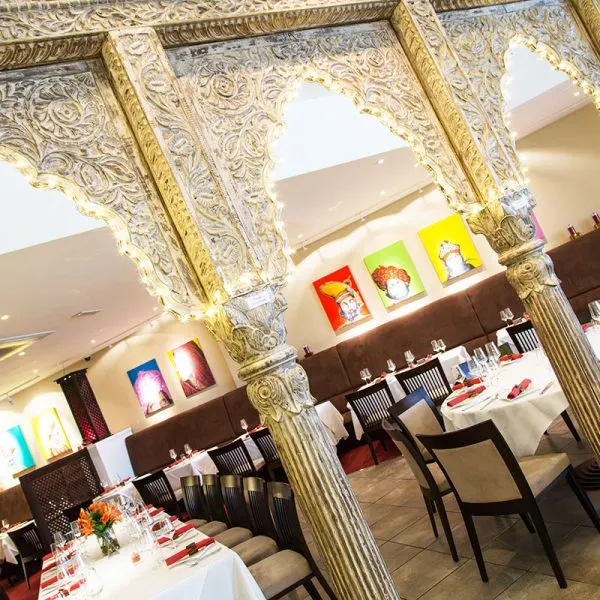 Ornate gilt archway frames an upscale restaurant dining area with colourful artwork on walls and white tablecloth tables.