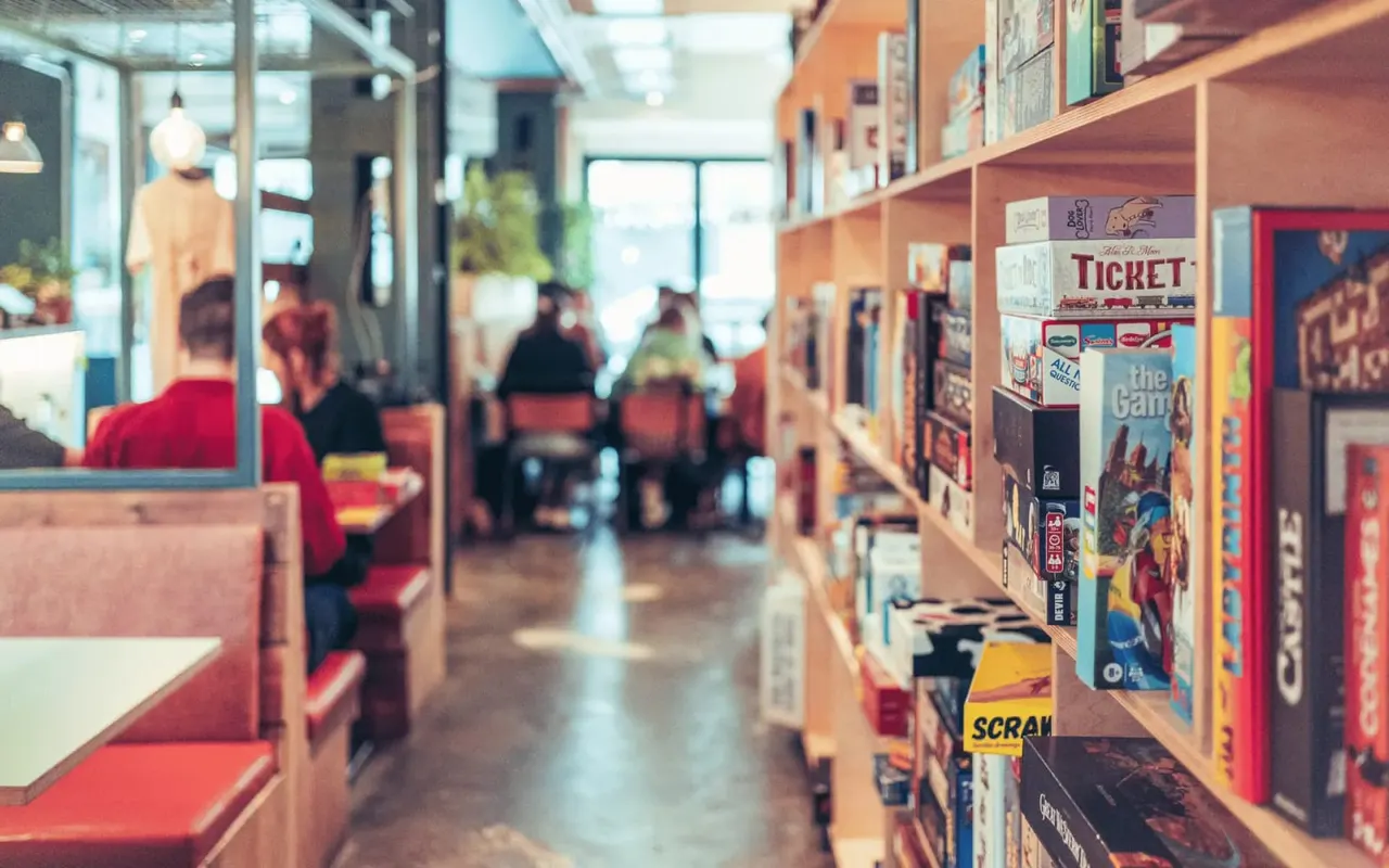 Interior of a board game café with shelves of games on display and visitors seated at tables.