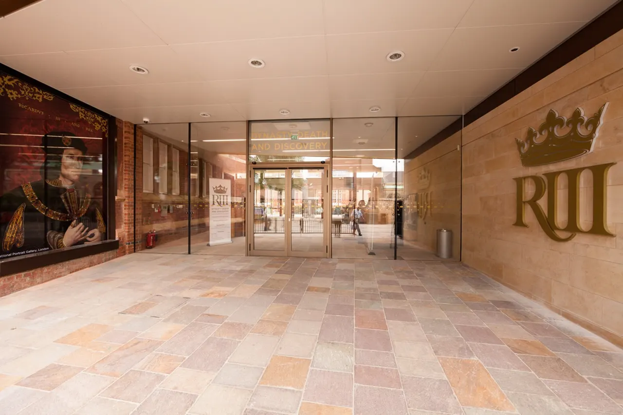 Empty entrance foyer with tiled flooring, glass doors, and gold crown signage for a historical visitor centre.