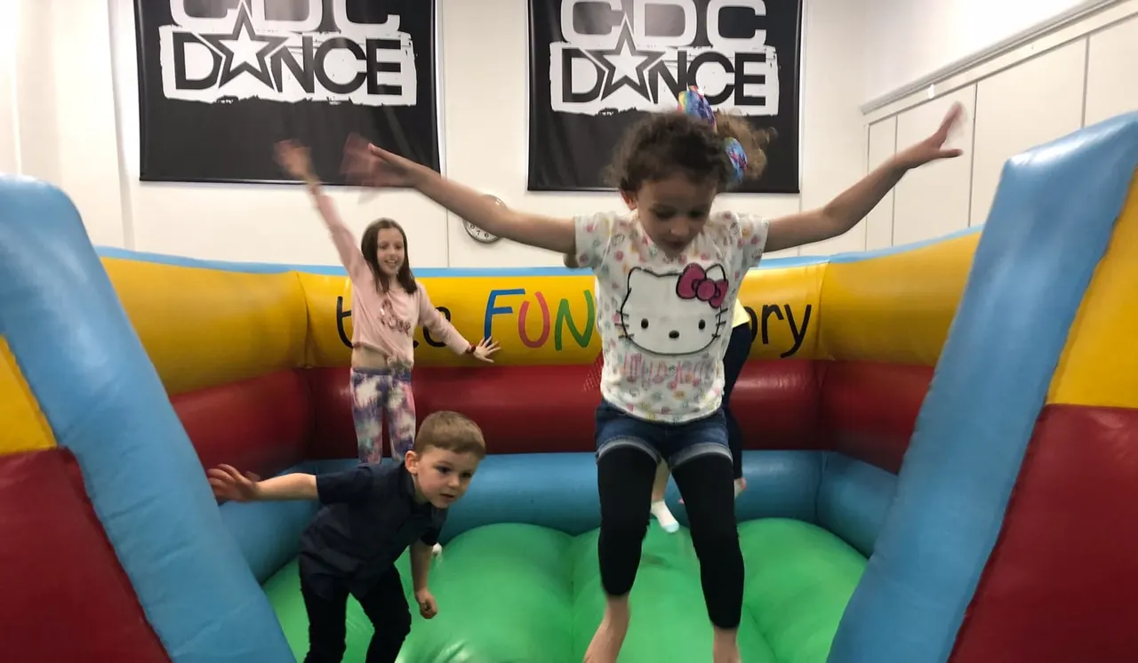 Young children playing on a colourful inflatable bouncy castle at an indoor dance facility.