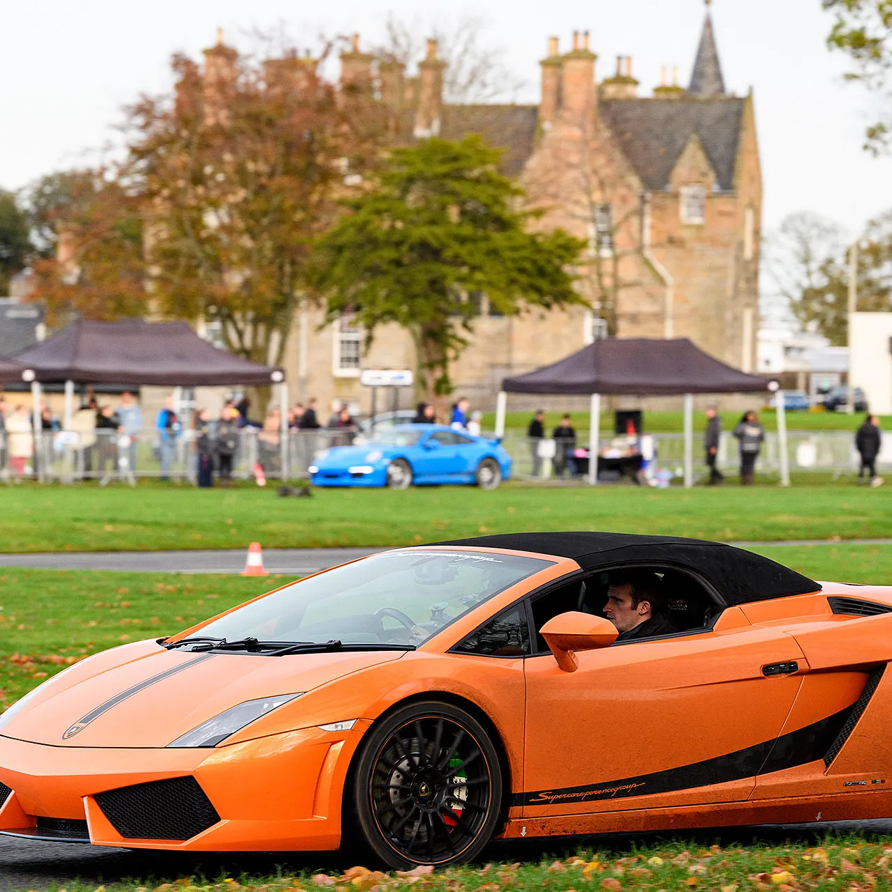 Sports car at outdoor motor show with castle and spectators in background.
