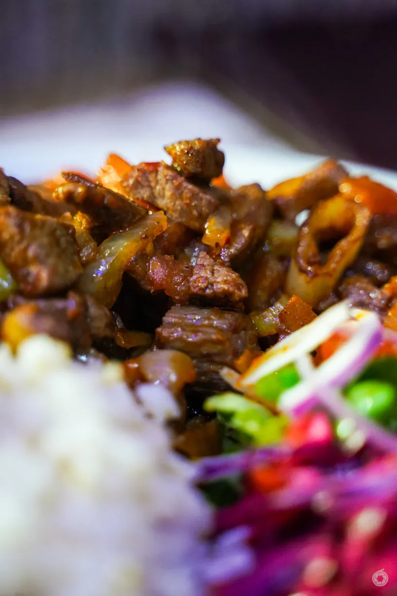Close-up of caramelised meat chunks with peppers and onions on a white plate.