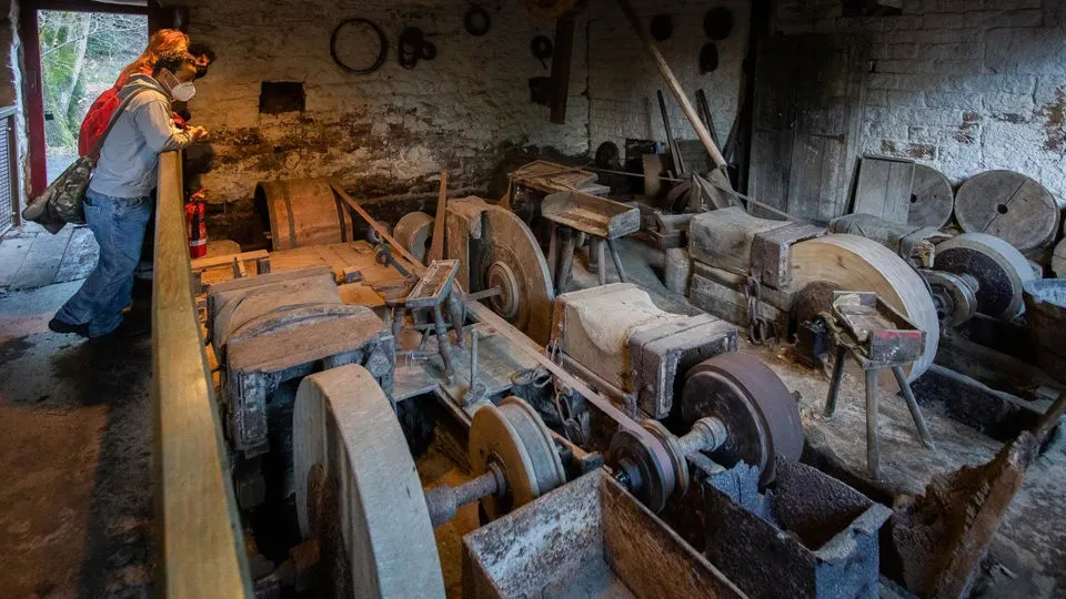 Visitor examining historic grinding wheels and machinery inside a stone mill building.