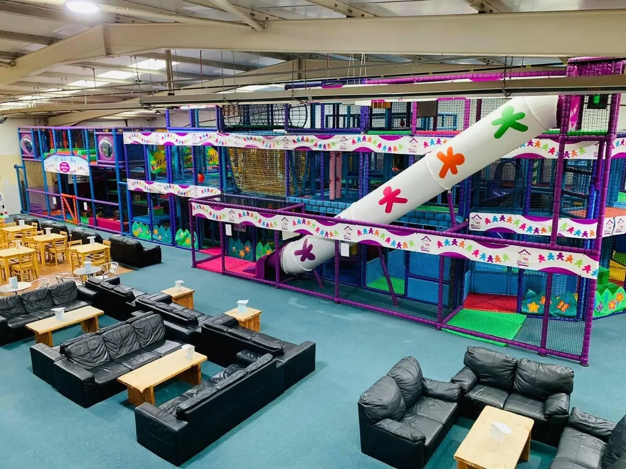 Indoor play area with colourful climbing structures, netting, and slides with seating areas in the foreground.