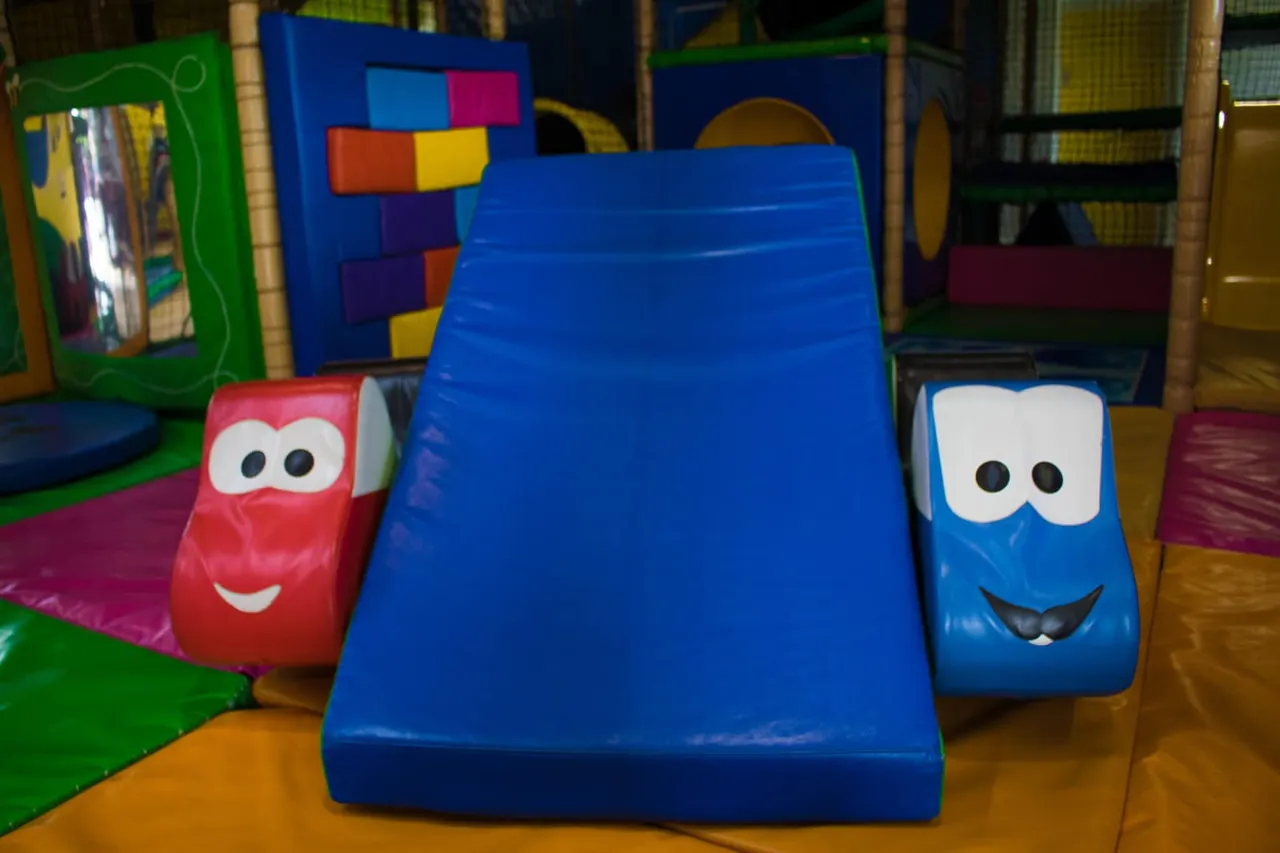 Colourful foam play equipment including a blue ramp and character-faced soft blocks in an indoor play centre.