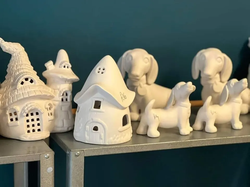 White ceramic figurines and decorative houses displayed on a shelf against a teal wall.