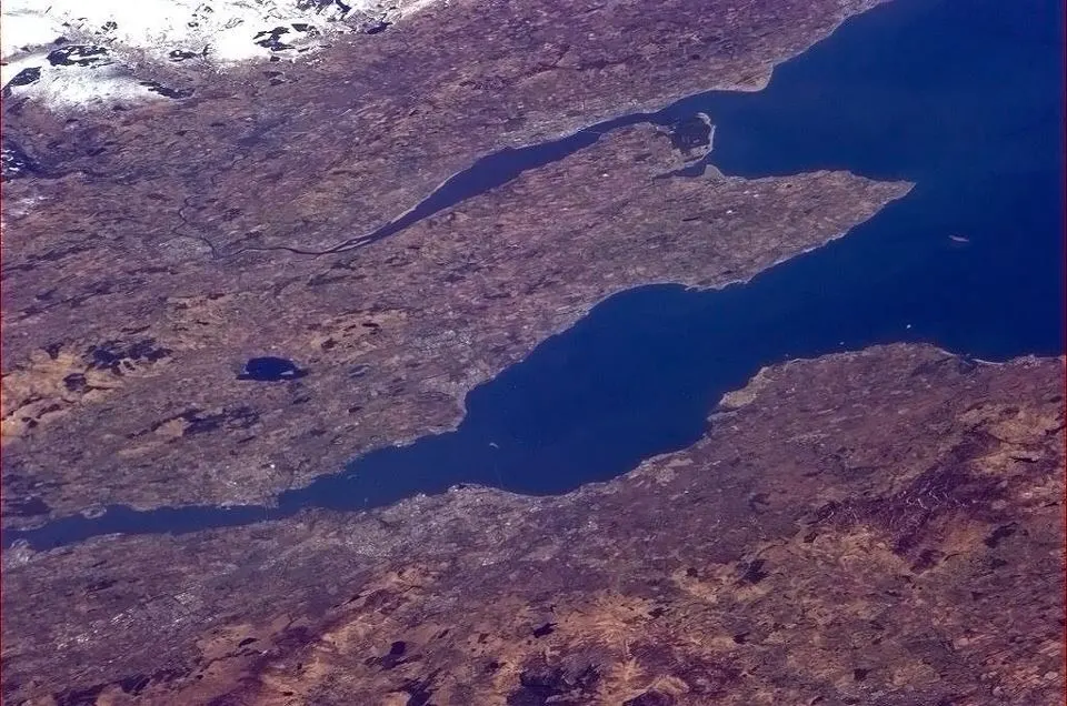 Aerial view of a winding lake or reservoir surrounded by moorland with patches of snow on higher ground.