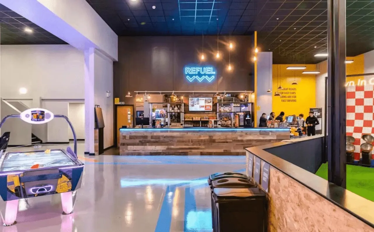 Modern indoor entertainment venue with air hockey table, service counter with neon 'REFUEL' sign, and arcade games.