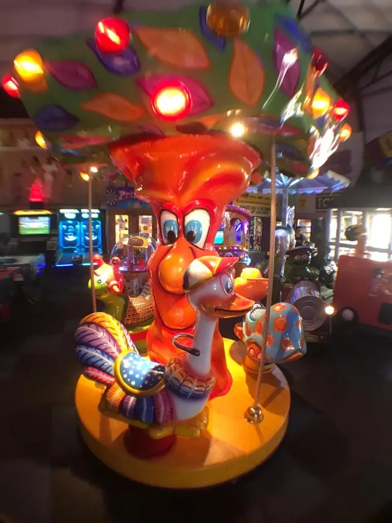Brightly lit arcade ride with a large red bird character and colourful illuminated decorations in an amusement arcade.