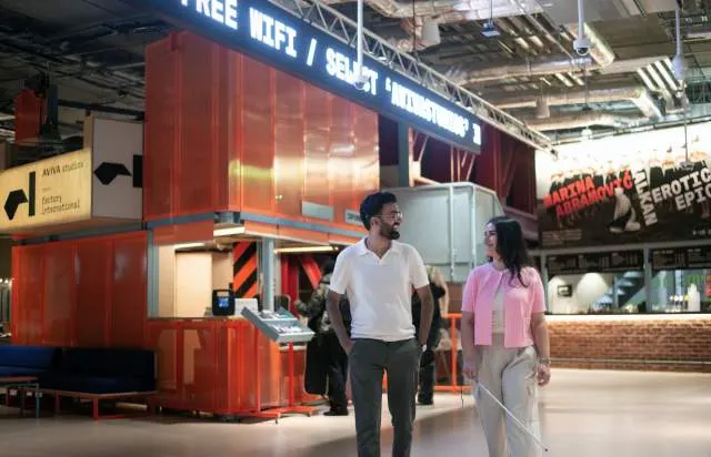 Two visitors walk through an indoor leisure facility with a red shipping container-style booth and signage overhead.