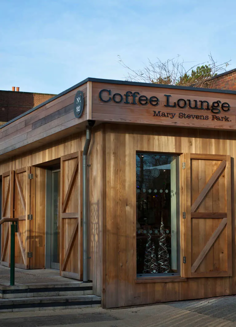 Wooden coffee lounge building with barn-style doors in a park setting under blue sky.