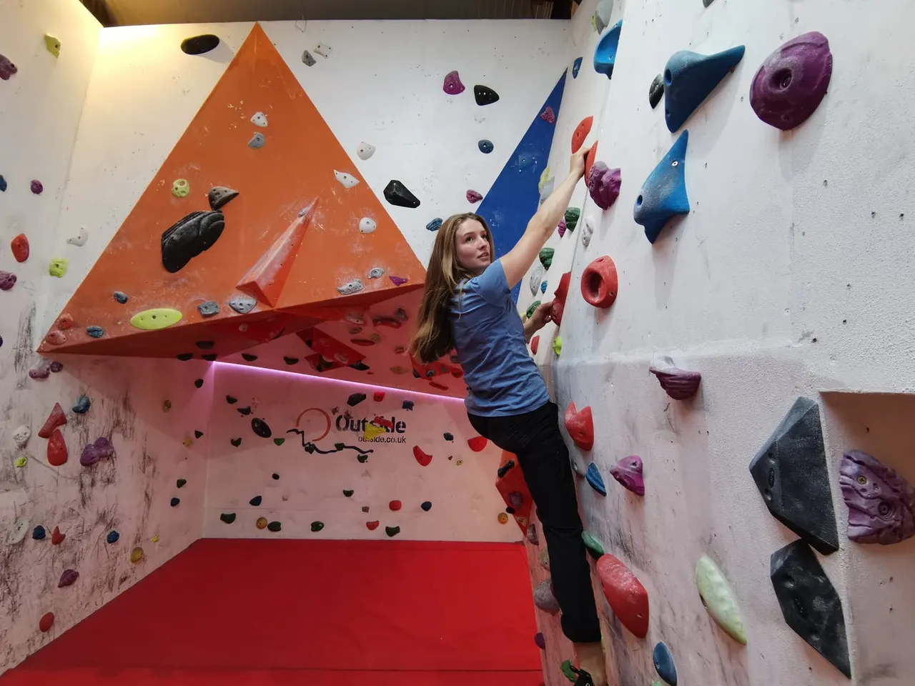 A young person indoor rock climbing on a wall with colourful holds and geometric painted sections.